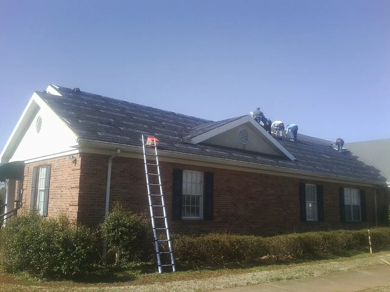 Crew tearing shingles off a brick ranch roof with a ladder set — Emergency Roof Repair work by our crew in Hackensack
